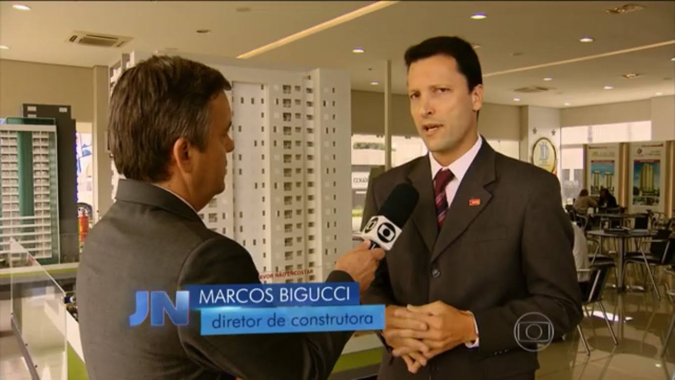 Entrevista em telejornal mostrando um repórter da TV Globo conversando com Marcos Bigucci de terno em ambiente corporativo com maquete de prédio ao fundo.